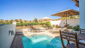 A pool area with lounge chairs and umbrellas, surrounded by a fence and a view of a vineyard.