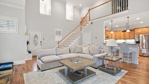 Amplia sala de estar con un sofá seccional grande, una mesa de centro y una escalera que conduce a un nivel superior.