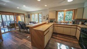 Eine geräumige Küche mit Holzboden, einem Essbereich mit Stühlen und großen Fenstern mit Blick ins Freie.