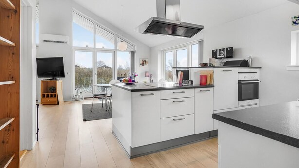 Een moderne keuken met witte kasten, een inbouwoven en een groot raam met uitzicht op een tuin.