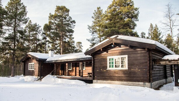 A wooden cabin with a porch and a window, surrounded by snow and tall trees. - Lovely home in Drevsjø with lake view (Engerdal)