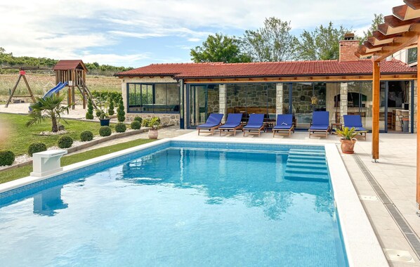 A swimming pool with lounge chairs, a covered seating area, and a children's play structure.
