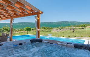 A hot tub with a view of a swimming pool and a mountainous landscape.