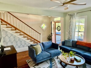 A living room with a staircase, blue sofas, a coffee table, and a ceiling fan.