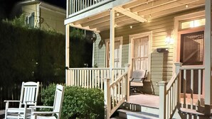 A two-story house with a porch, a small outdoor seating area with chairs, and a visible front door.