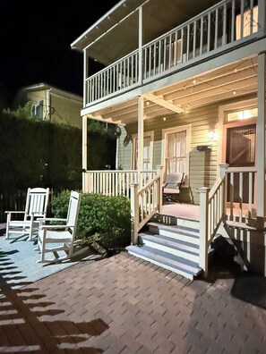A two-story house with a porch, a small outdoor seating area with chairs, and a visible front door.