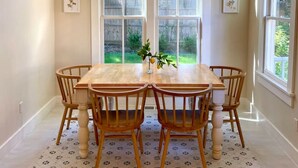 A dining room with a large table and chairs, a chandelier, and large windows with a view of the outdoors.