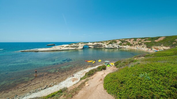 A coastal landscape with clear waters, rocky cliffs, and a sandy beach.
