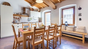A cozy kitchen with wooden beams, a dining area with a bench, and a view of the outside through a window.