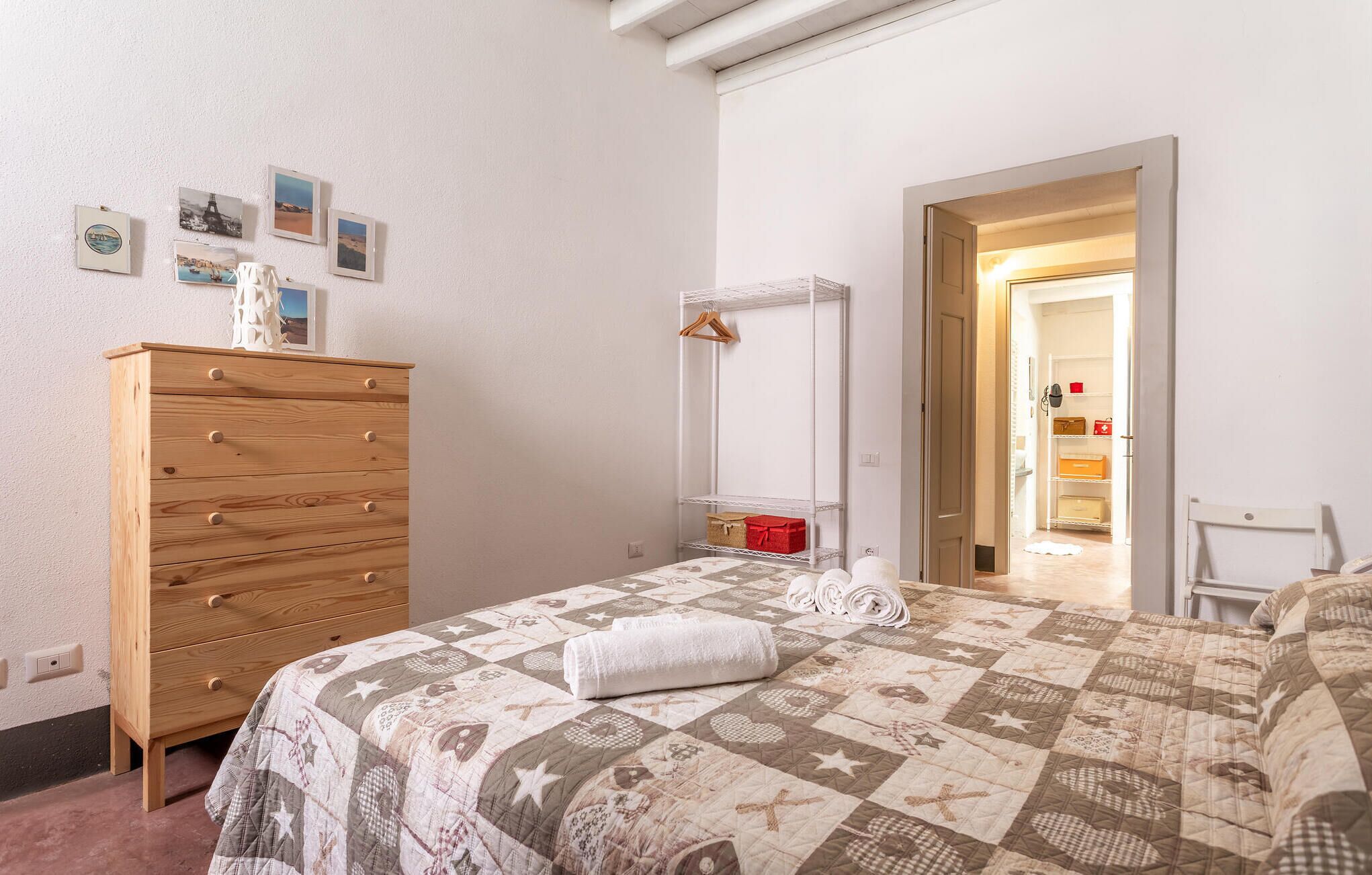 A bedroom with a wooden dresser, a quilted bedspread, and a walk-in closet with shelves.