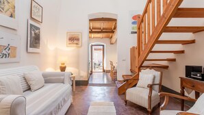 A cozy living room with a sofa, chairs, a wooden staircase, and artwork on the walls.