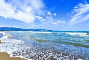 Ein Strand mit Wellen, blauem Himmel und Bergen im Hintergrund.
