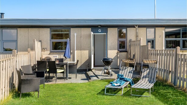 Eine Terrasse mit Gartenmöbeln, einem Grill und einer Tür mit dem Buchstaben 'G'.