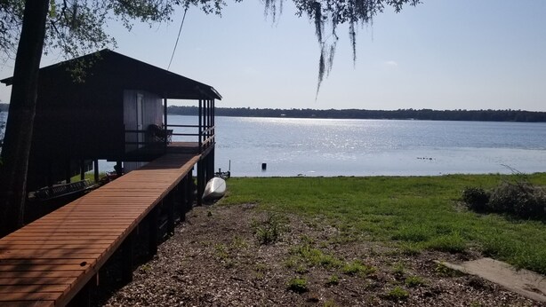 Un pontile in legno che conduce a una struttura coperta, affacciato su un lago con una vista limpida dell'acqua.