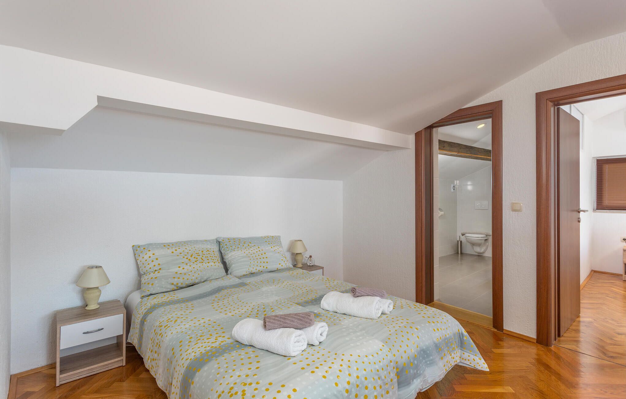 A bedroom with a bed, nightstand, and a bathroom visible through an open door.