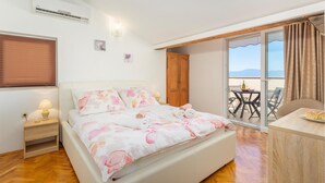 Quarto com cama, mesa de cabeceira, guarda-roupa de madeira e varanda com mesa e cadeiras.