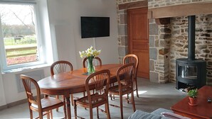 Un comedor con una mesa y sillas de madera, un florero con flores, una pared de piedra y un estufa de leña.