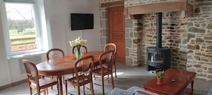 Un coin repas avec une table et des chaises en bois, un vase de fleurs, un mur en pierre et un poêle à bois.