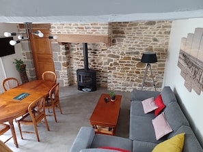 Un salon chaleureux avec un mur en pierre, une table à manger en bois, un canapé et une cheminée.