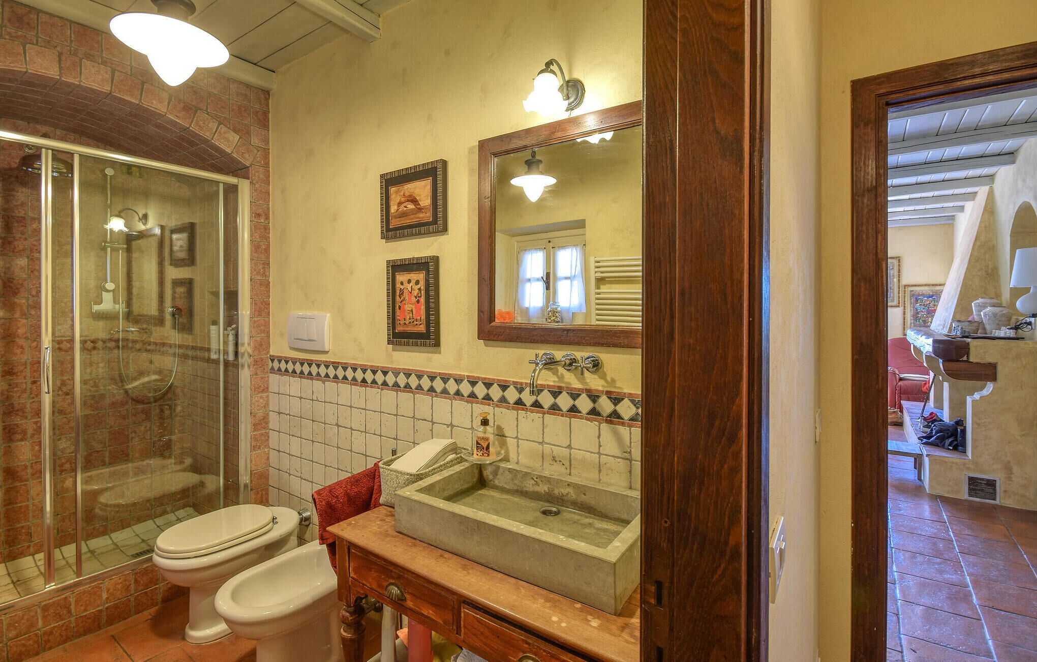 Un baño con ducha de vidrio, dos inodoros, un lavamanos y un espejo.