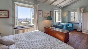 Un dormitorio con una cama grande, un aparador de madera, un sofá azul y vistas de la ciudad a través de las ventanas.