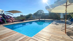Una piscina con muelle de madera, rodeada de sombrillas y plantas en macetas.