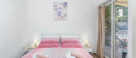 A bedroom with a bed, two bedside lamps, a window with a view of greenery, and a painting on the wall.