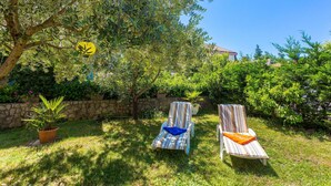 Two striped lounge chairs in a garden with a stone wall and a tree.