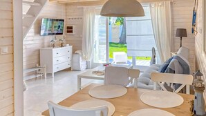A modern, well-lit room with a wooden dining table, white chairs, and a large window offering a view of the outdoors. - 2 bedroom cozy home in Miedzywodzie (Miedzywodzie)