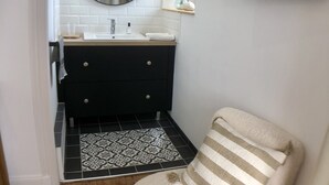 A bathroom with a black and white tiled floor, a black vanity with a mirror, a white sink, and a beige chair with striped cushions. - Perrosian villa with Jacuzzi, Sauna, Hammam, Home Cinema (Perros-Guirec)
