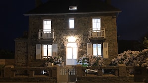 A stone building with a central door, two balconies, and a lit entrance. - Perrosian villa with Jacuzzi, Sauna, Hammam, Home Cinema (Perros-Guirec)