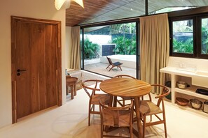 A modern interior with a wooden dining table and chairs, a white console table with kitchenware, and a view of a patio with a chair and plants.