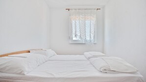 A single-bed room with white bedding, a wooden headboard, and a window with sheer curtains.