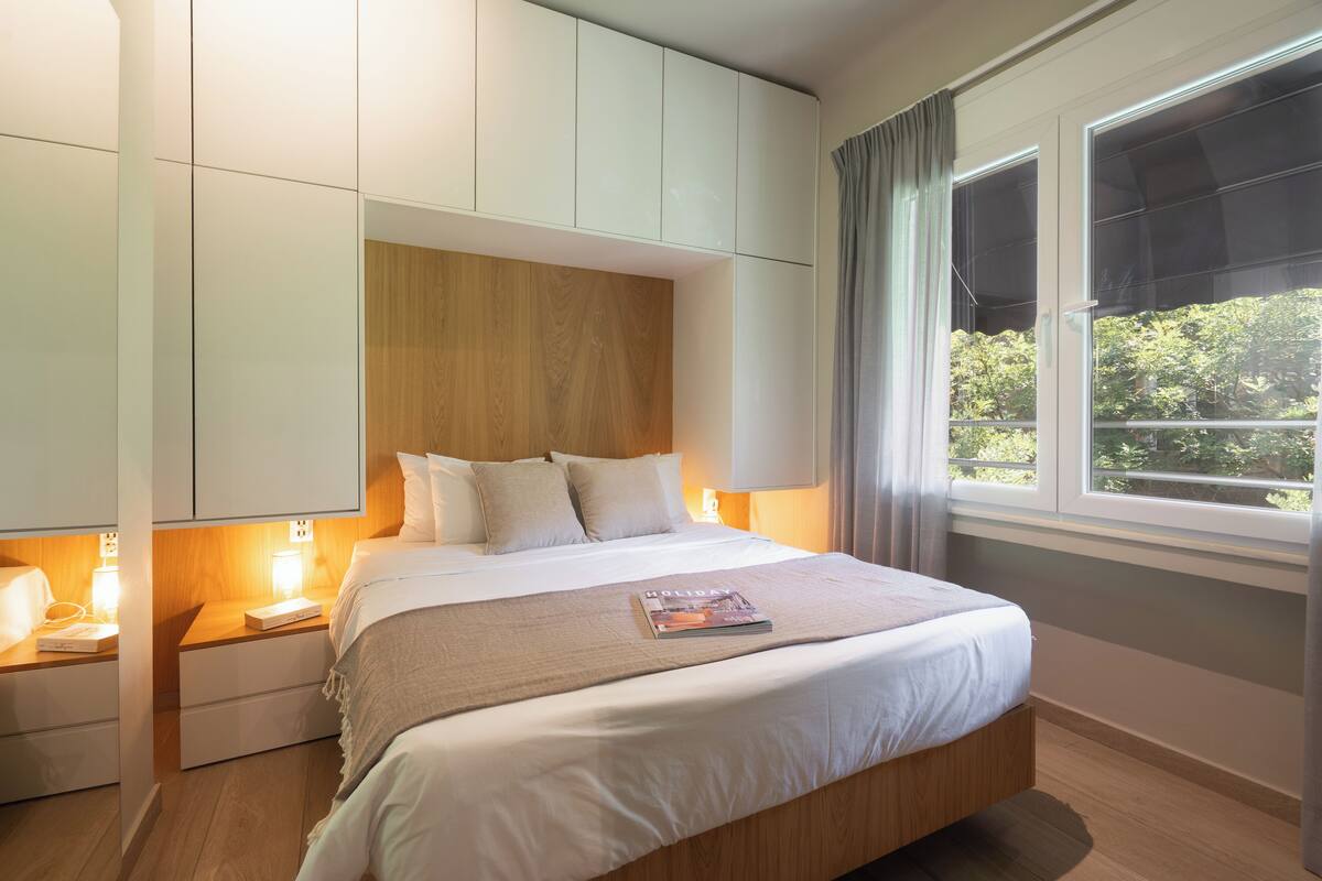 Ein Schlafzimmer mit einem Bett, Nachttischen, einem Holzkopfteil und einem Fenster mit Vorhängen.