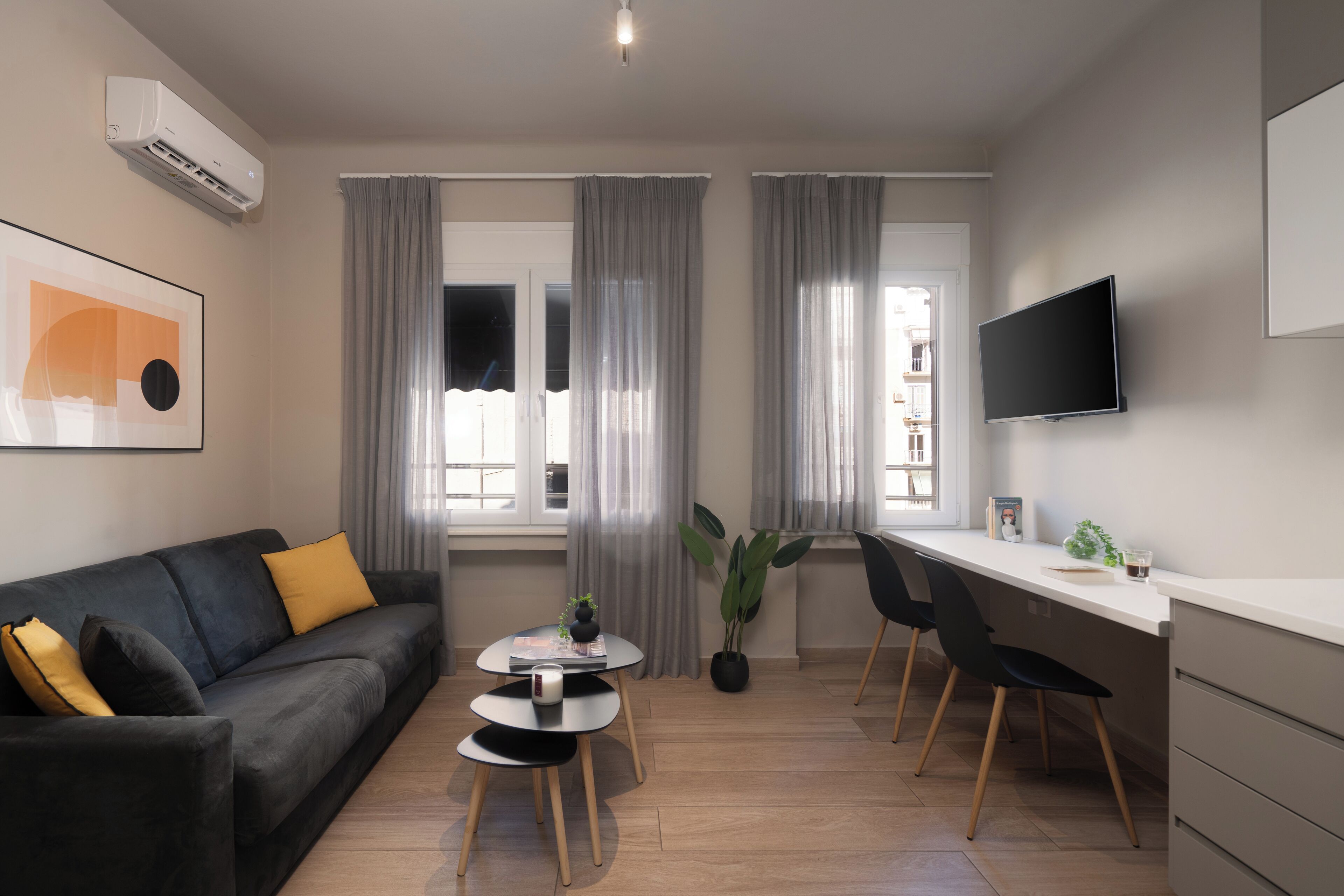 Una sala de estar moderna con un sofá, una mesa de centro, un comedor con sillas, un televisor de pantalla plana y una planta en maceta.
