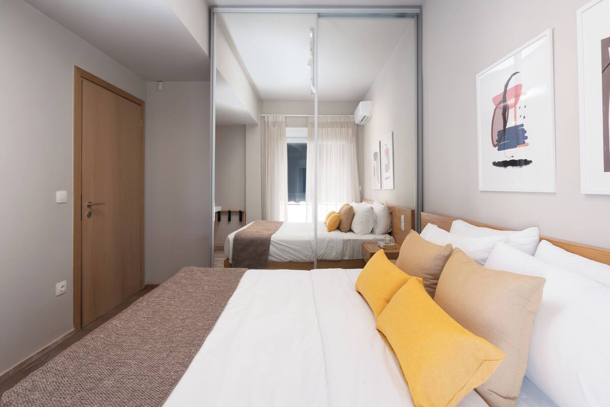 Ein Hotelzimmer mit einem großen Bett, einem Nachttisch, einem Spiegel und einem Fenster mit Vorhängen.