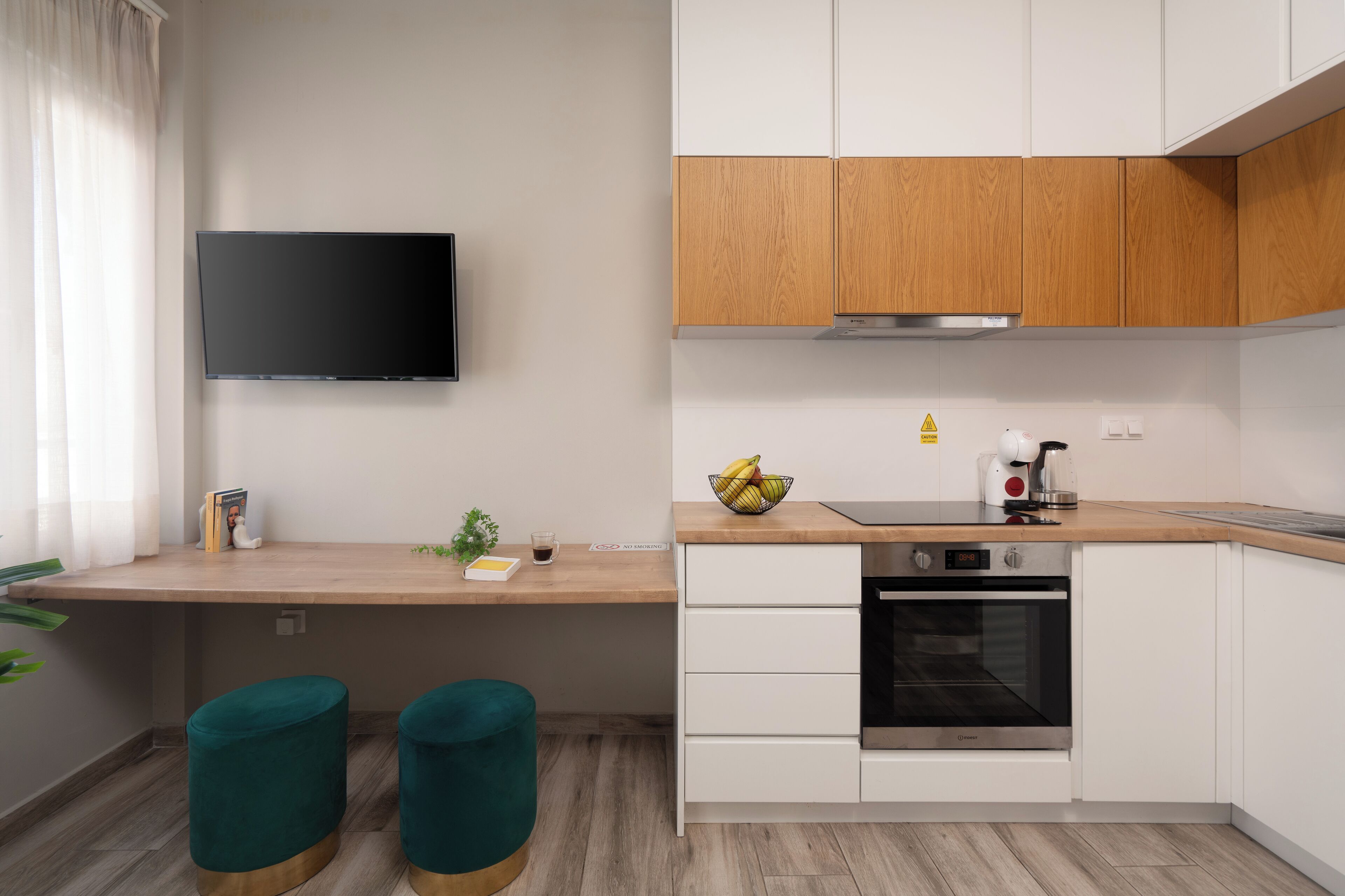 A modern kitchen with white cabinets, a wooden countertop, a built-in oven, and a flat-screen TV mounted on the wall.