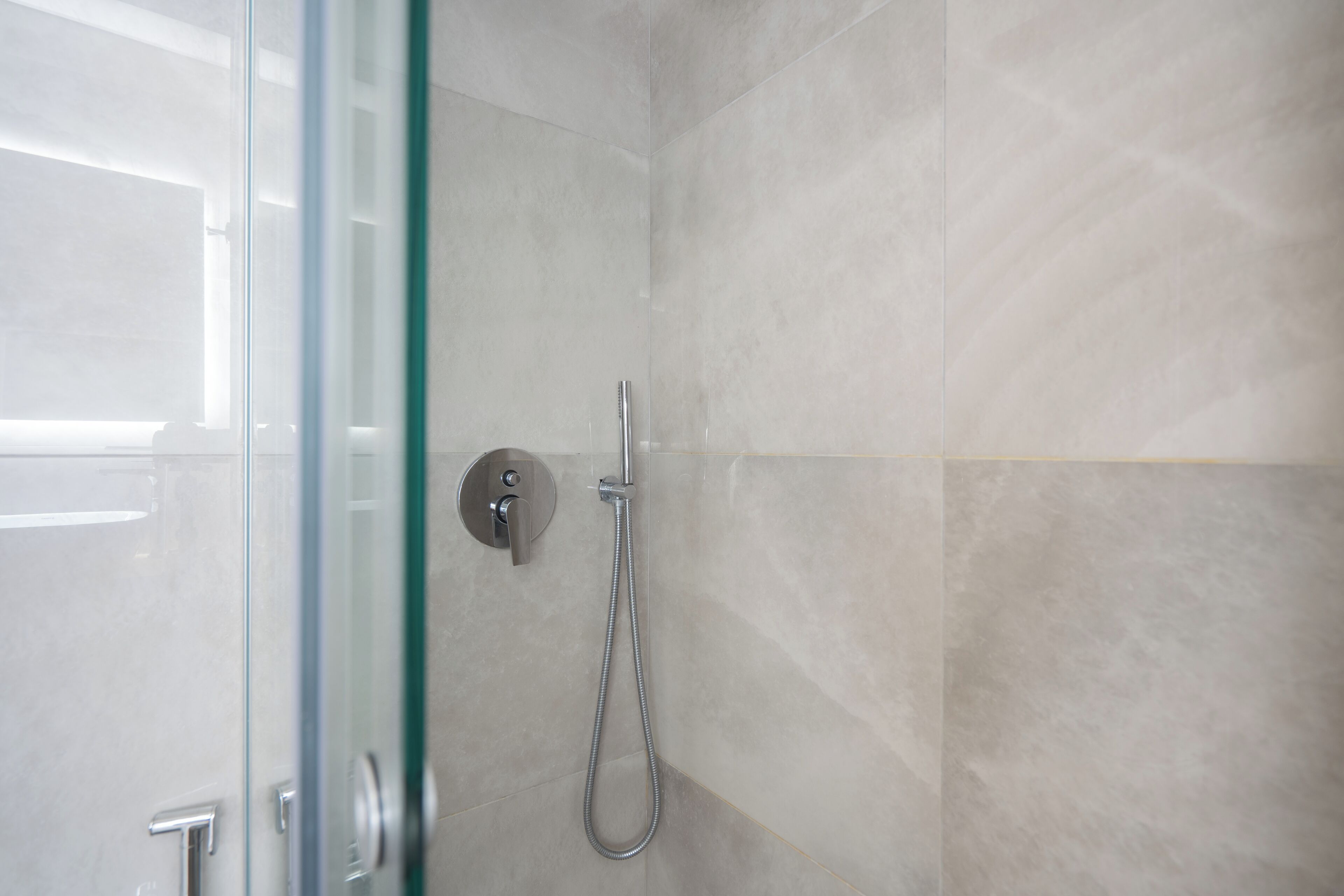 Een douchecabine van glas met een handdouche en een bedieningspaneel aan de muur.
