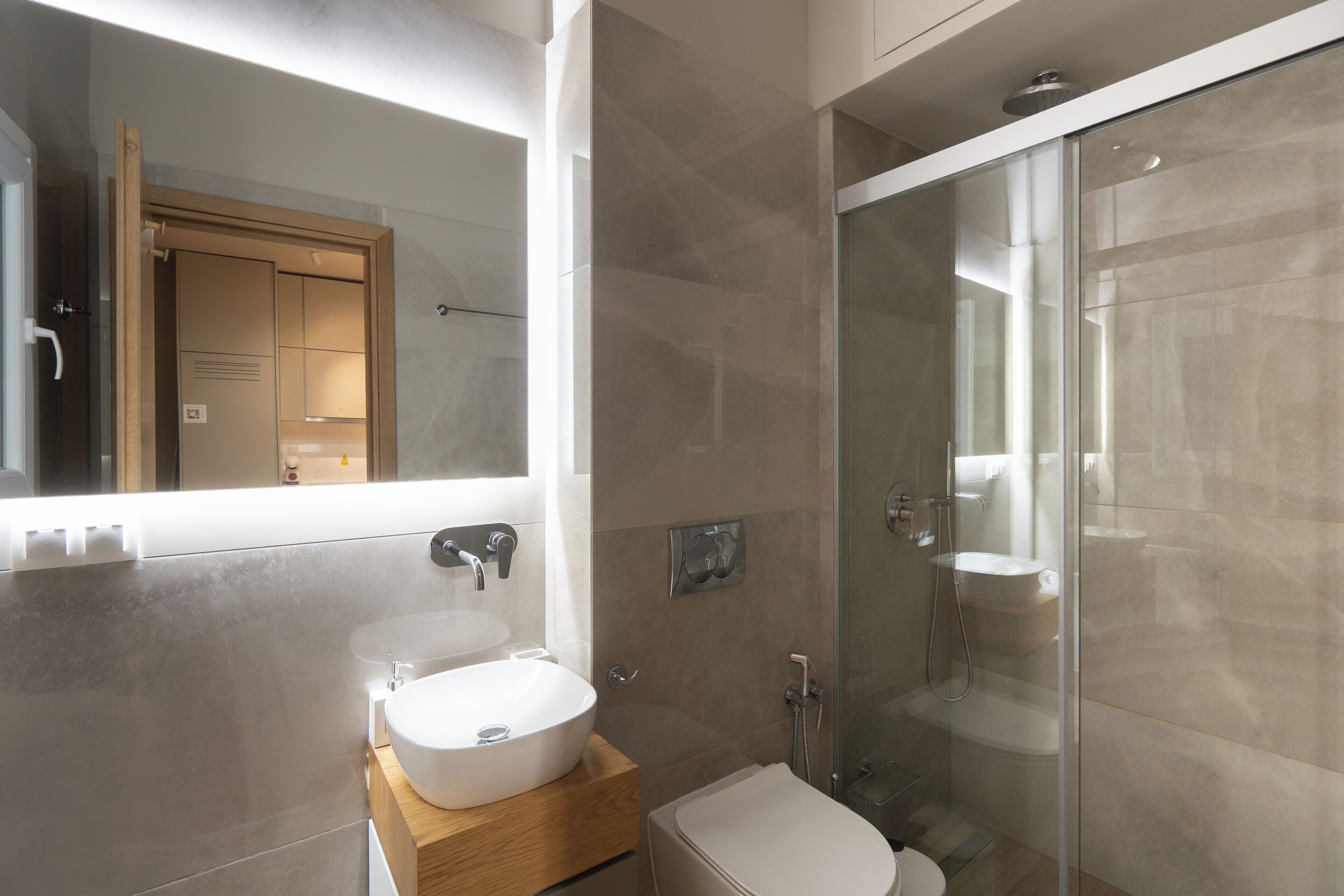 Un baño moderno con un espejo grande, un lavabo blanco y una ducha con mampara de vidrio.