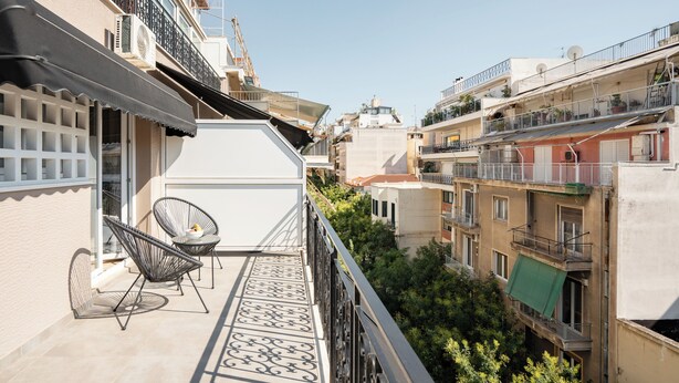 Een balkon met twee stoelen, een klein tafeltje en uitzicht op omliggende gebouwen.