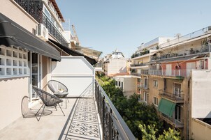 Uma varanda com duas cadeiras, uma mesa pequena e vista para edifícios vizinhos.