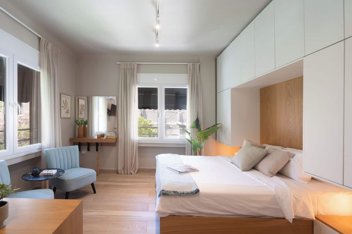 Ein modernes Schlafzimmer mit einem Bett, einem Sessel, einem Schreibtisch und einem großen Fenster.