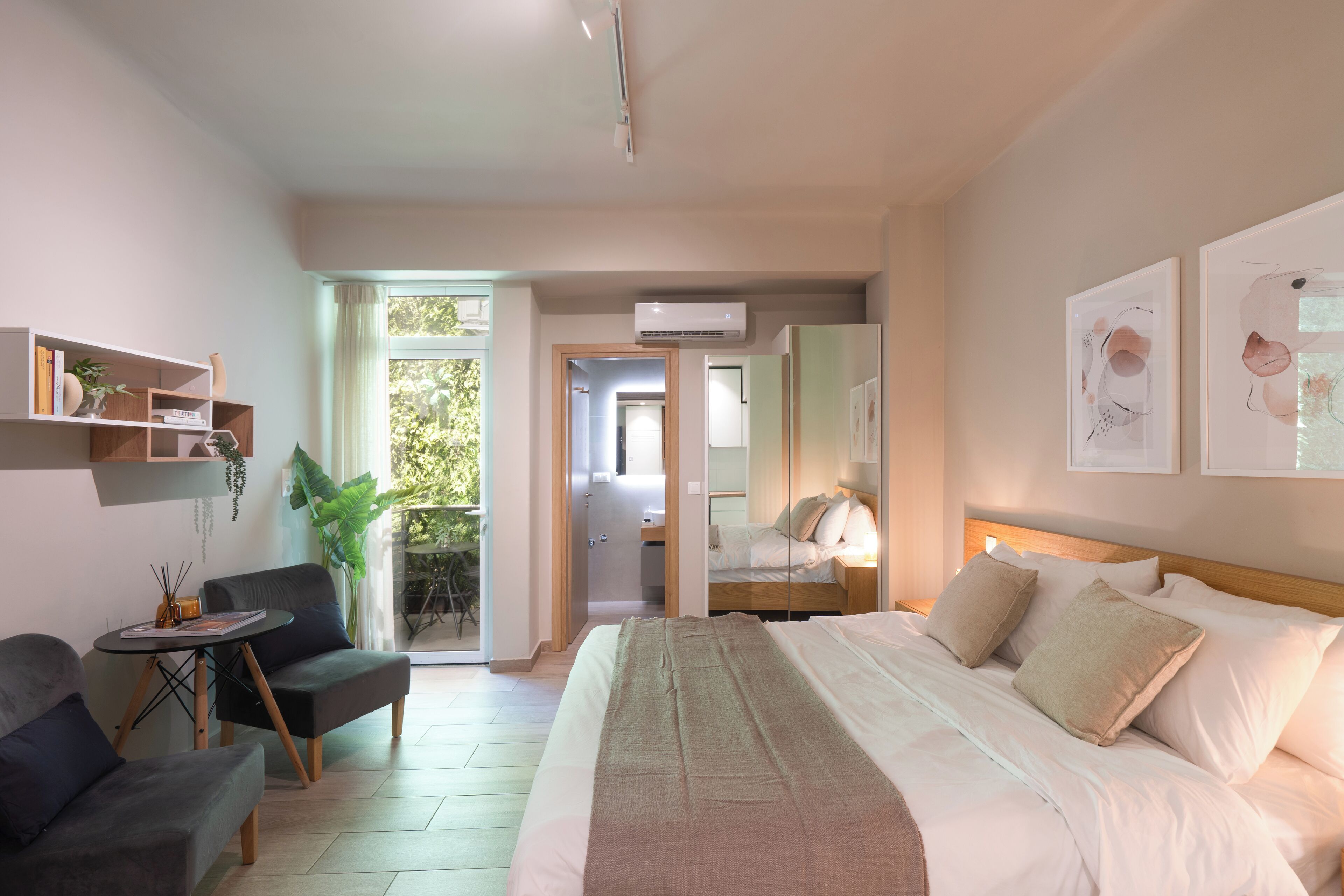 Une chambre d’hôtel moderne dotée d’un grand lit, d’un coin salon avec un fauteuil et une table, d’une petite table d’appoint et offrant une vue sur l’extérieur grâce à une porte vitrée.