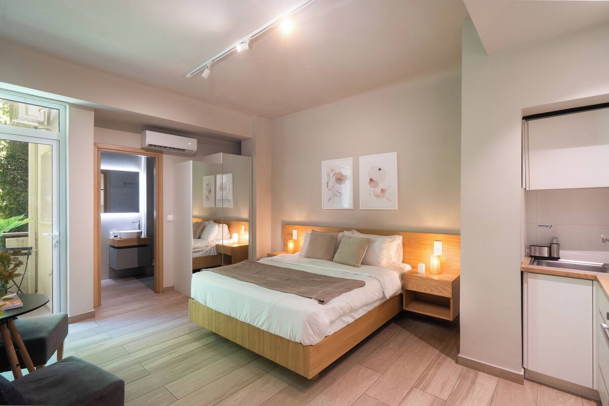 Ein modernes Schlafzimmer mit einem großen Bett, Nachttischen, einer eingebauten Garderobe und einer kleinen Küchenzeile.