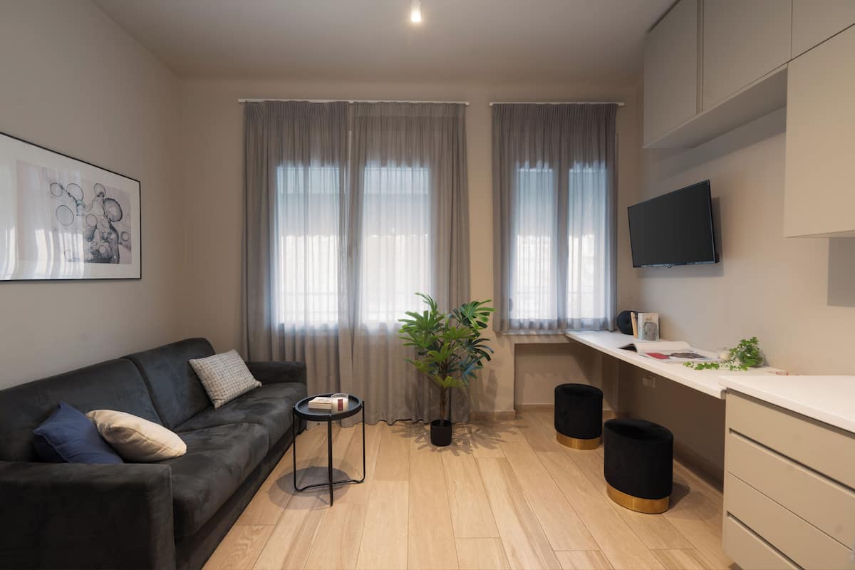 Ein modernes Wohnzimmer mit einer Couch, einem kleinen Beistelltisch, einer Zimmerpflanze und einem an der Wand befestigten Flachbildfernseher.