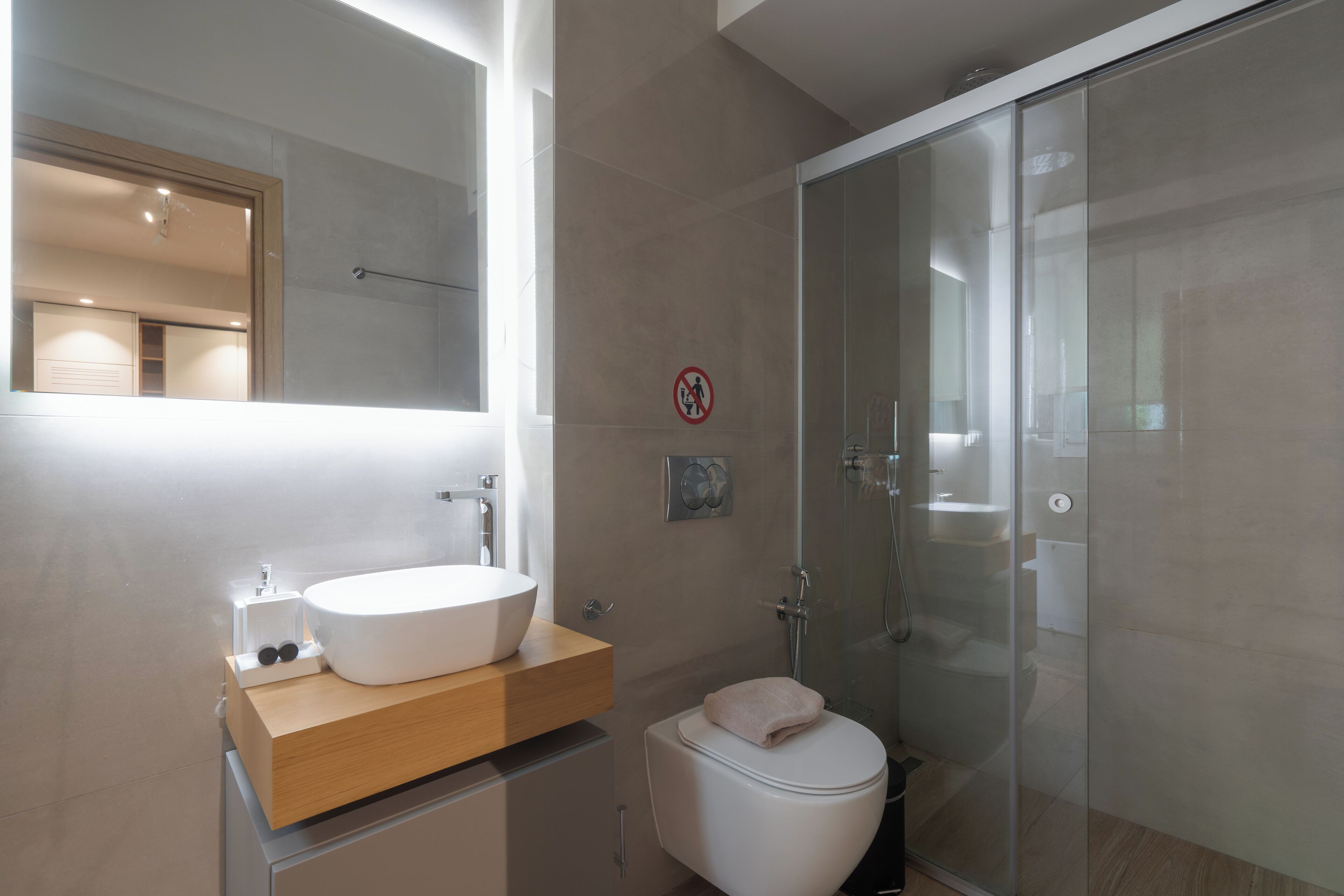 A modern bathroom with a large mirror, a white sink, a glass shower enclosure, and a toilet.