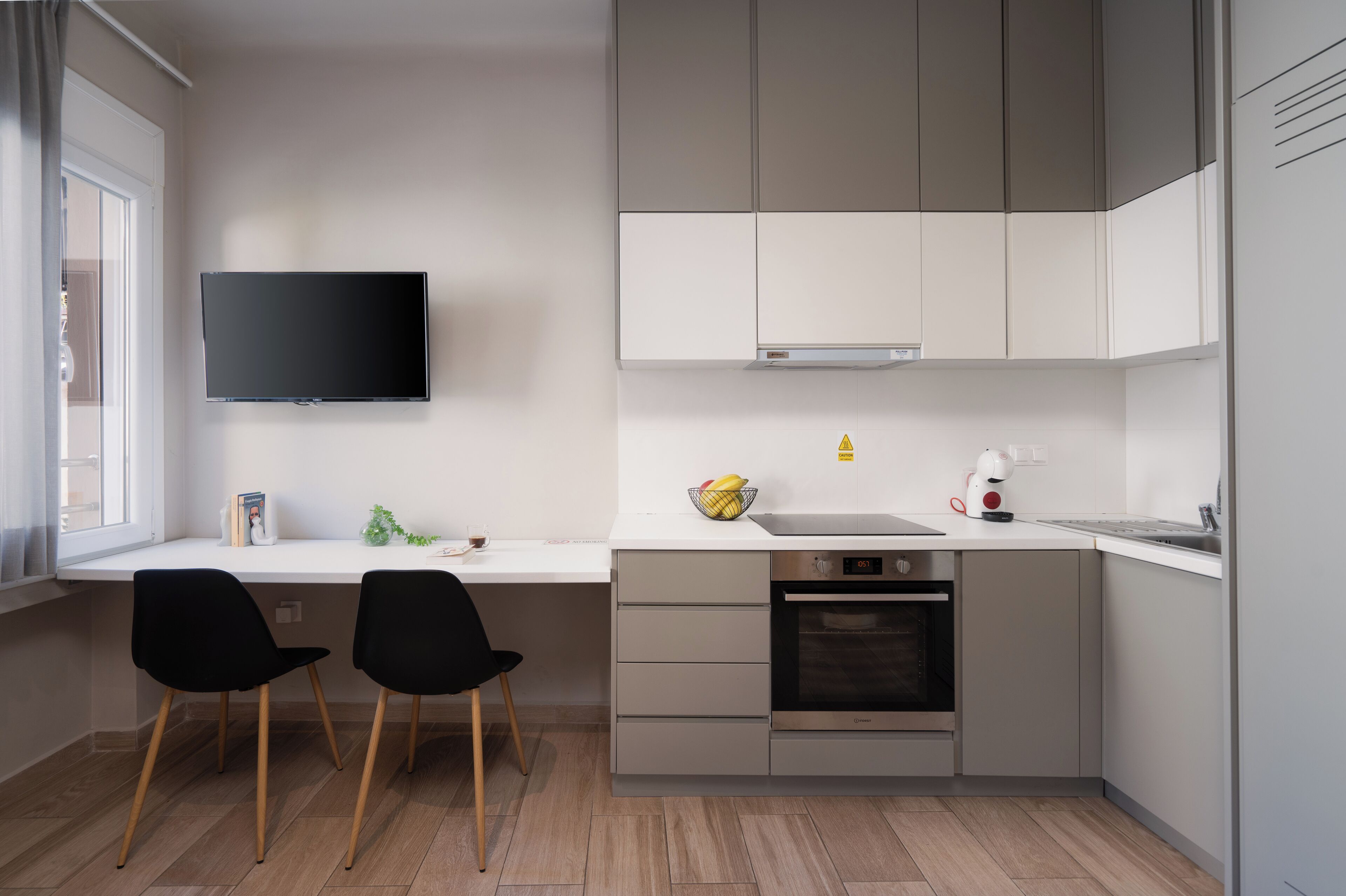 A modern kitchen with a flat-screen TV, two black chairs, a sink, and a built-in oven.