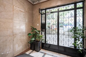 Uma entrada moderna com uma grande placa informativa sobre a Rua Didotou, uma planta em vaso e um portão de ferro decorativo.