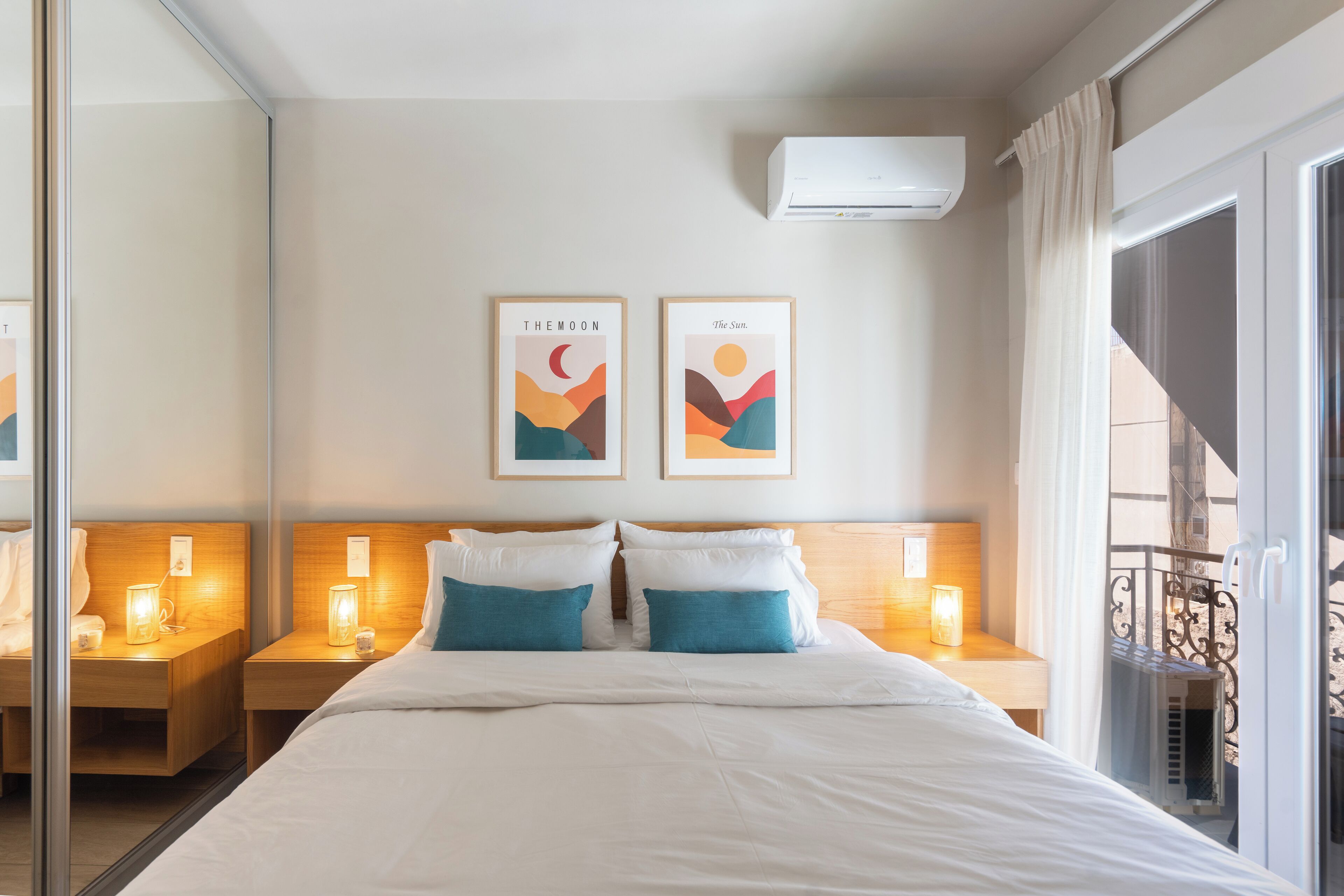 A hotel room with a large bed, two bedside tables with lamps, a mirror, and artwork depicting the moon and sun on the wall.
