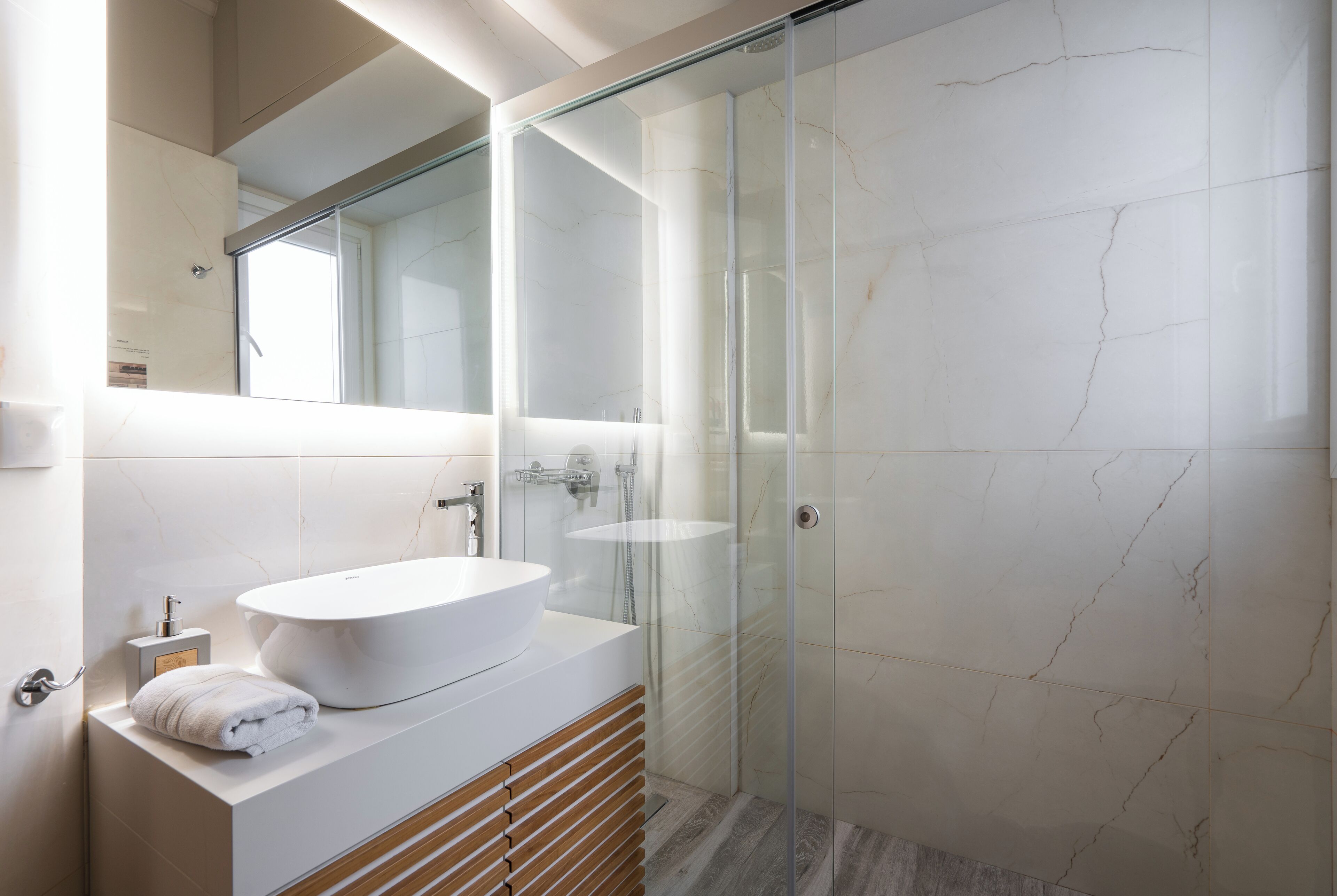 A modern bathroom with a large white sink, a glass shower enclosure, and a marble-tiled shower area.
